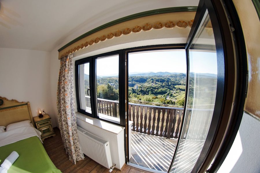 Cameră cu ușă largă spre balcon și vedere peste dealuri